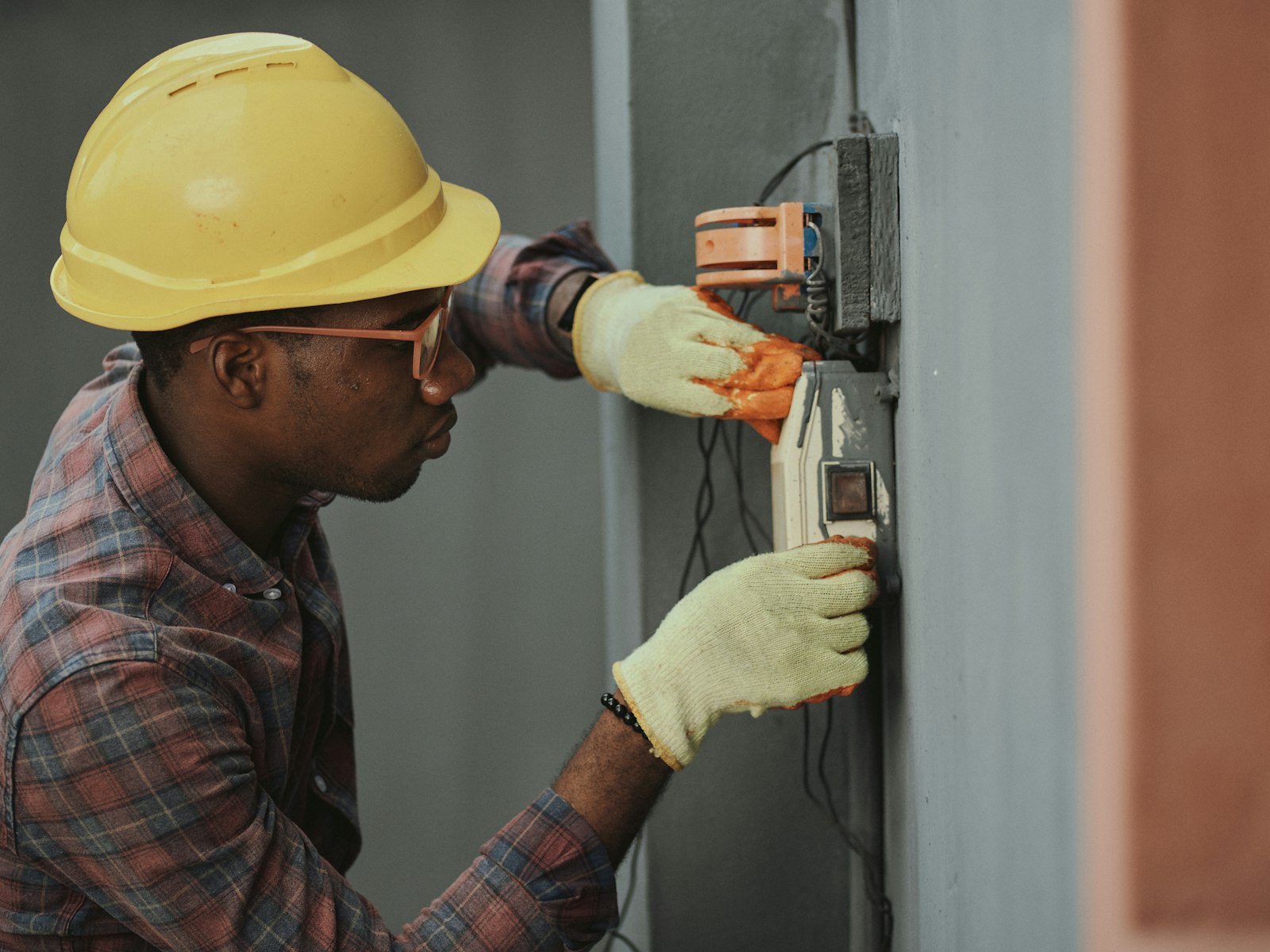 Técnico con casco y guantes revisando el conexionado de un registro eléctrico en fachada.
