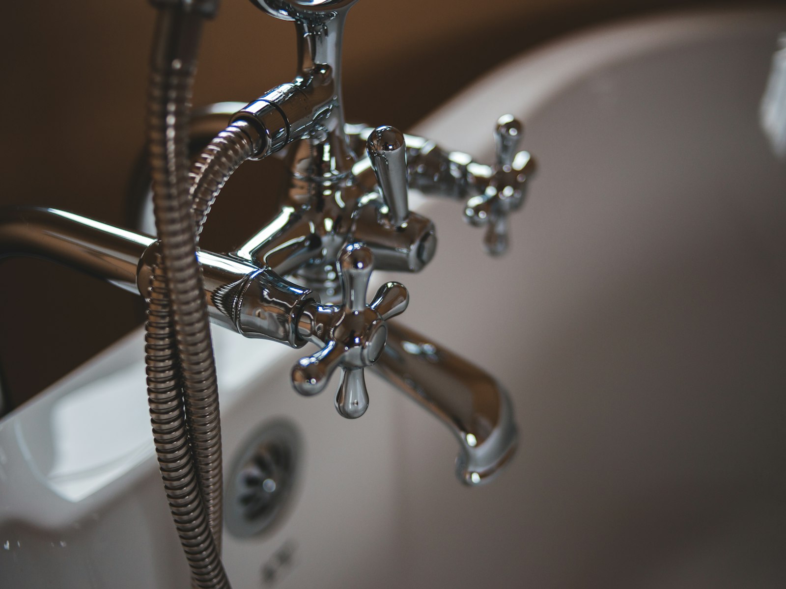 Detalle de grifería cromada de bañera con mando de dos volantes y ducha de teléfono.
