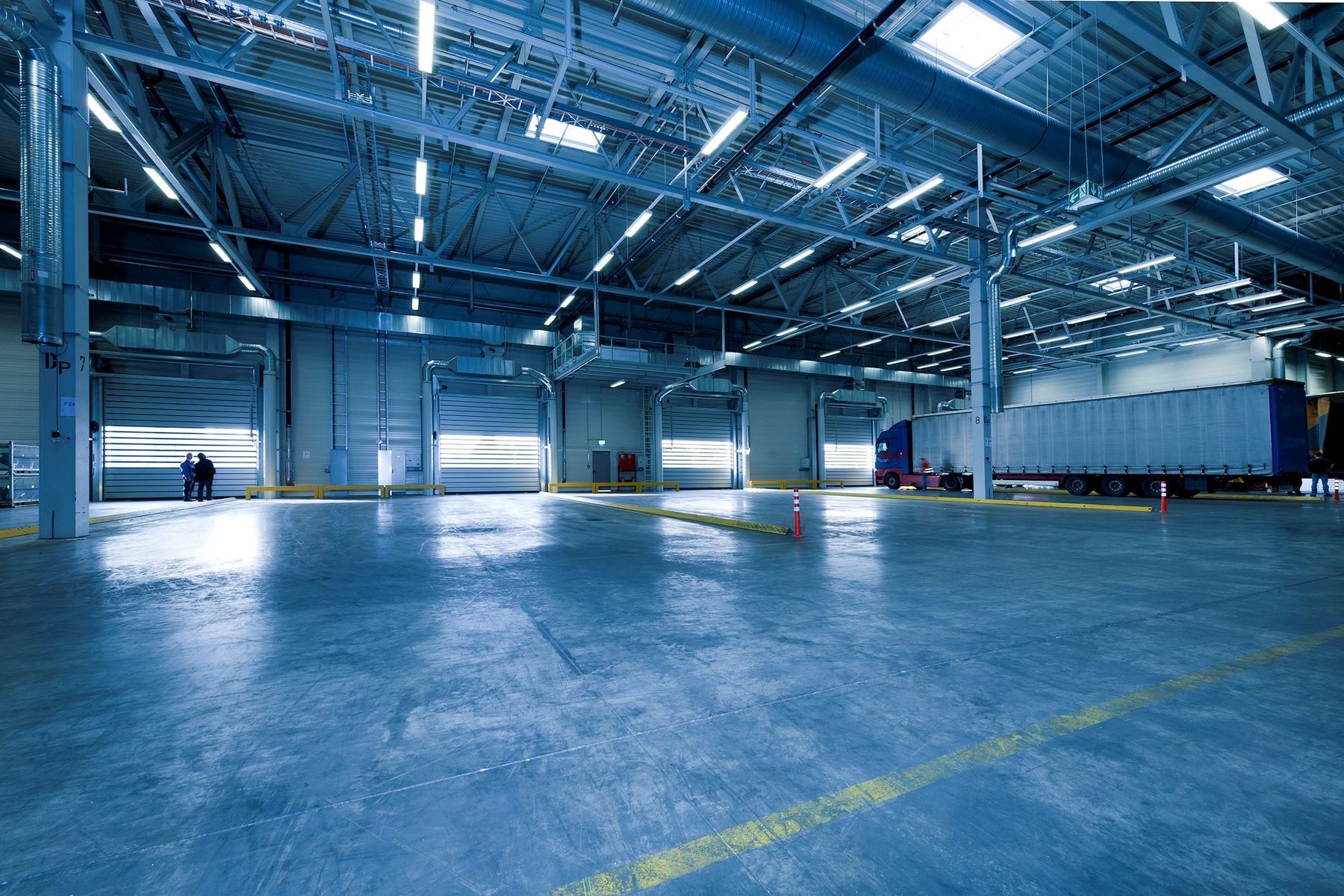 Nave industrial con conductos de climatización y ventilación en el techo, muelles de carga e instalaciones vistas.